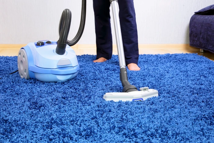Close-up of cleaning a plush blue carpet with a vacuum